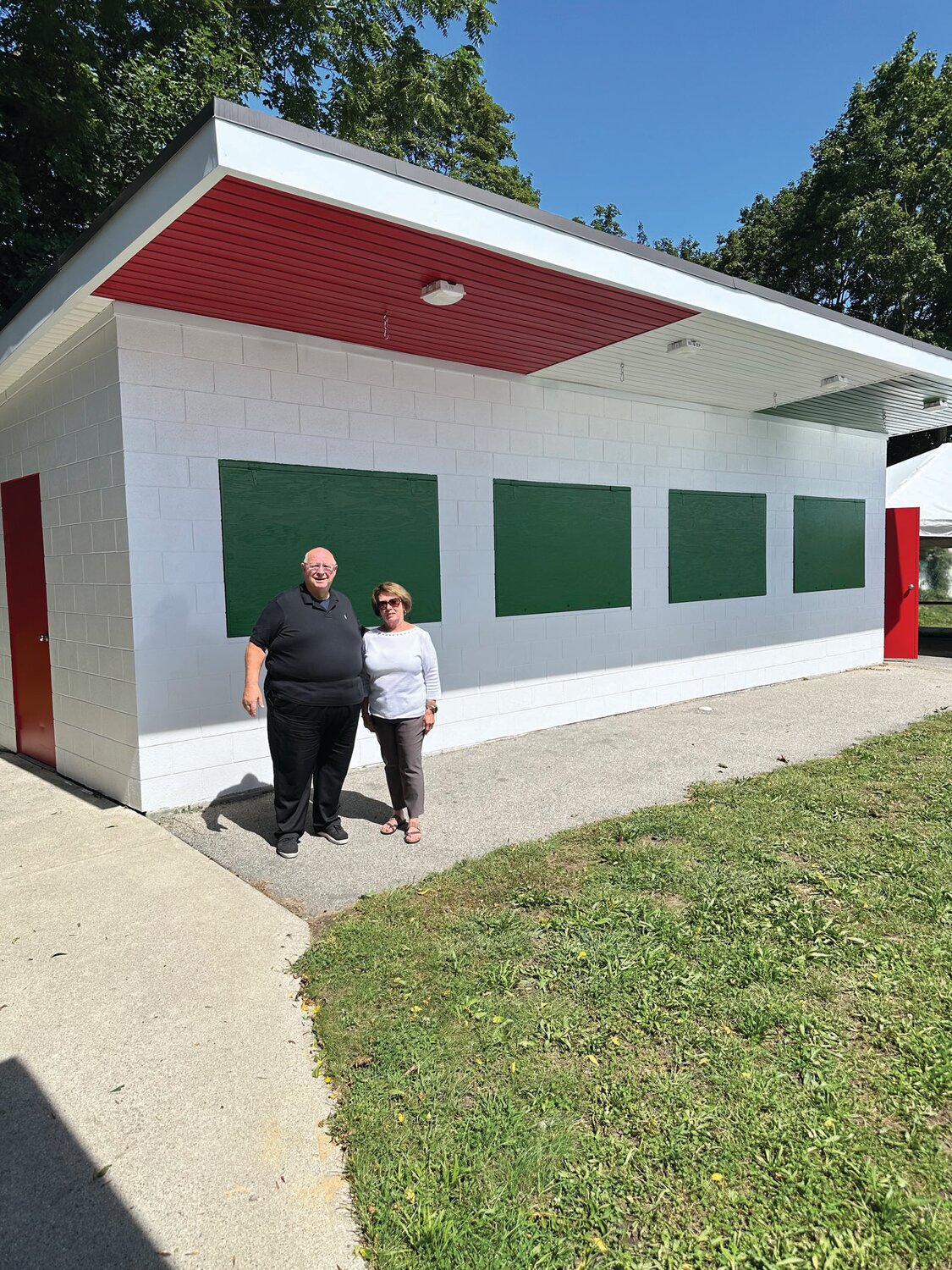 PROUD PALS: Rev. Peter J. Gower and Feast Chairperson Joanne Burley are smiling while standing under one of the newly painted food buildings where volunteer cooks will serve a variety of delicious Italian food through Sunday.
